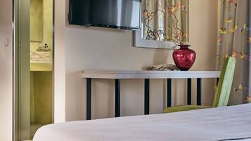 Habitación de hotel con cama, televisor montado en la pared, una mesita con un jarrón y cortina estampada con pájaros.