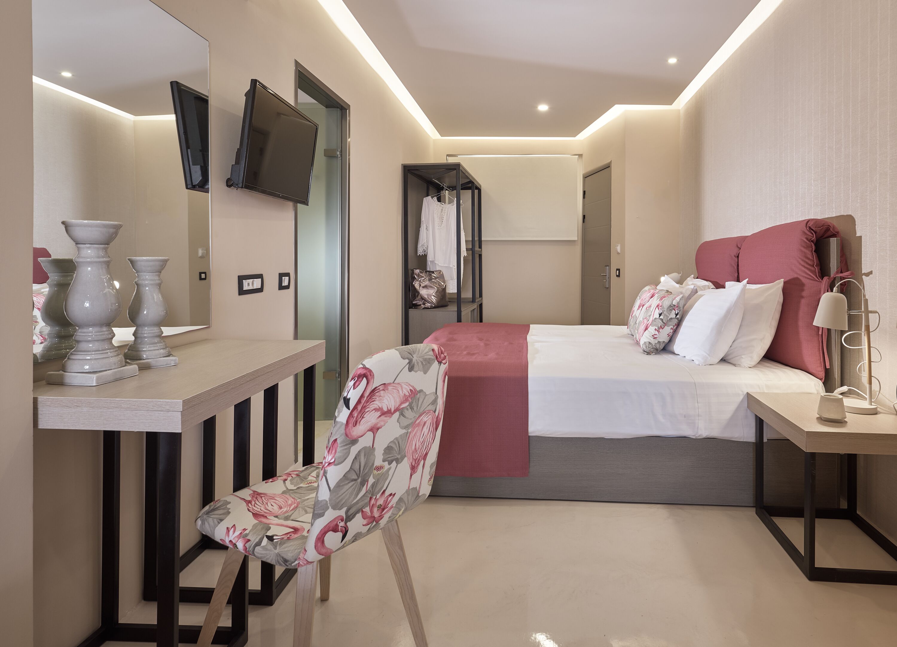 Ein modernes Hotelzimmer mit Bett, Nachttisch, Sessel und einem an der Wand befestigten Fernseher.