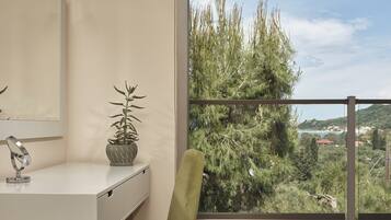 Un bany modern amb un lavabo blanc, una cadira verda, i vista a arbres i un paisatge llunyà a través d'una finestra gran.