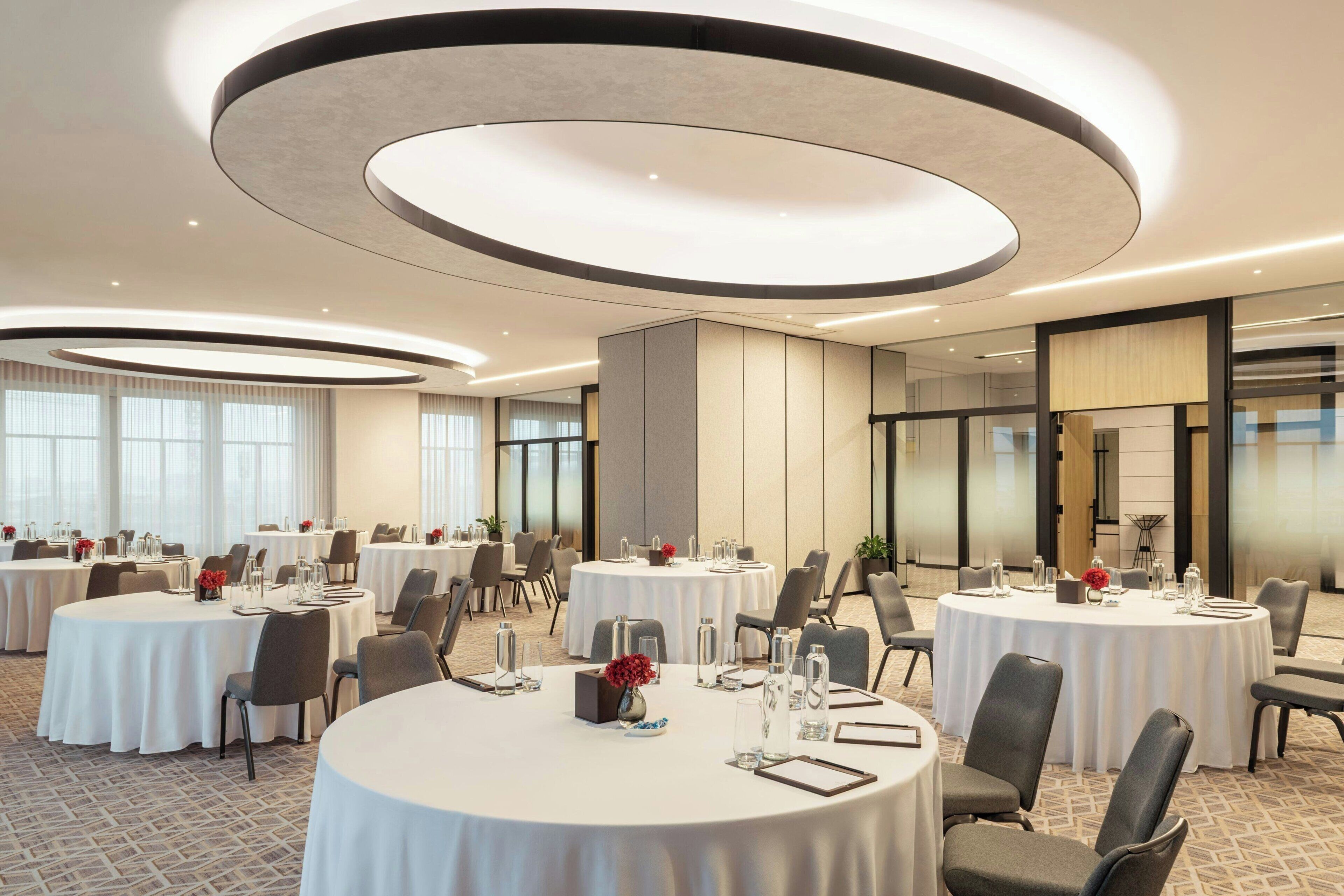 Un salón de conferencias con mesas redondas, sillas y un diseño moderno de techo.