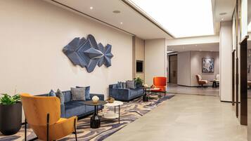 A modern lobby with a blue sofa, a wooden chair, and a patterned rug.
