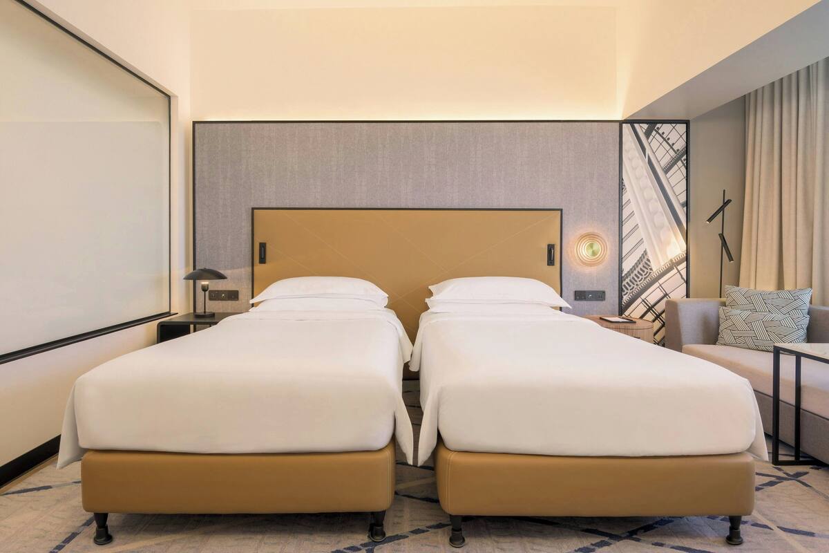 Een hotelkamer met twee bedden, een bank, een lamp en uitzicht op een gebouw.