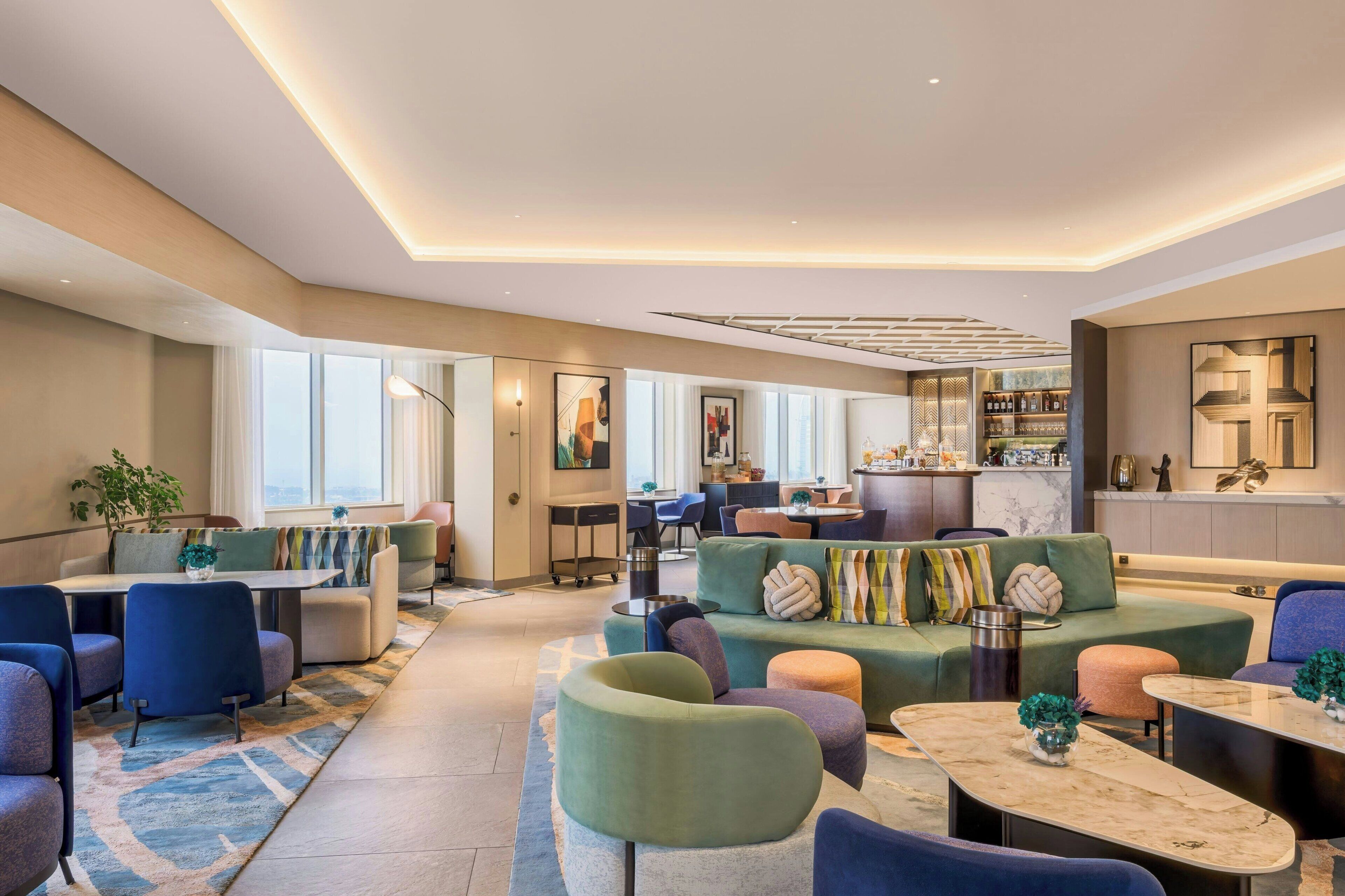 A modern hotel lobby with seating areas, a bar, and a dining space.