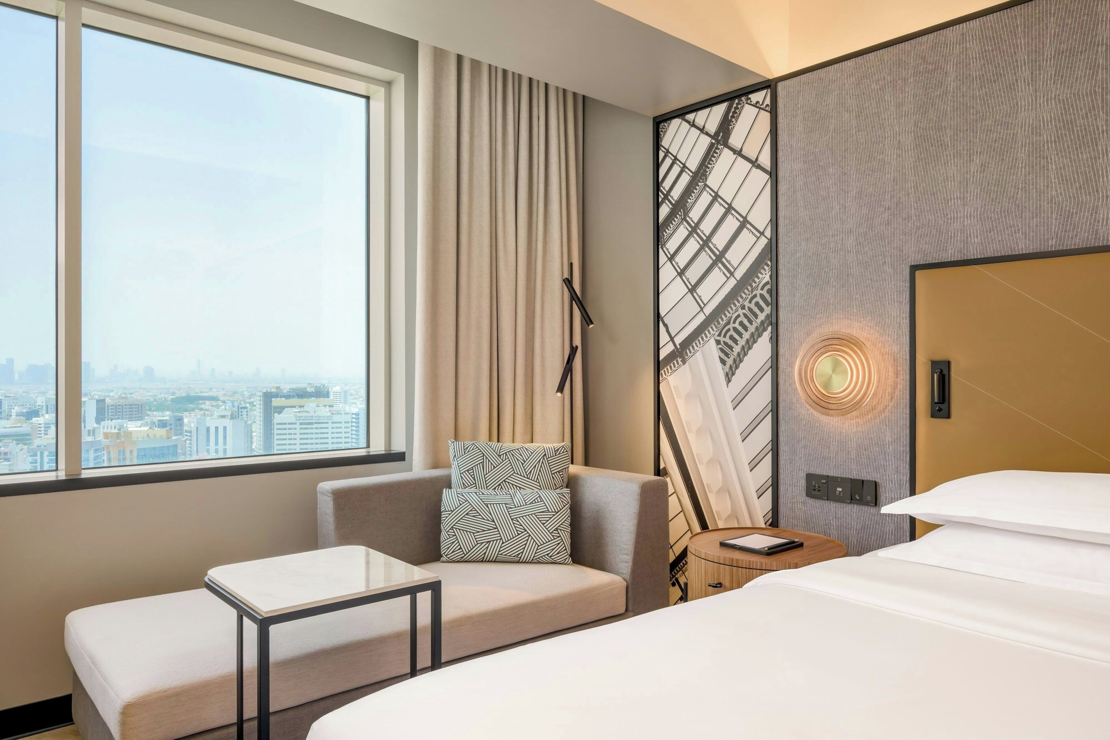 Ett hotellrum med ett stort fönster, en soffa, en säng och en väggmonterad lampa.