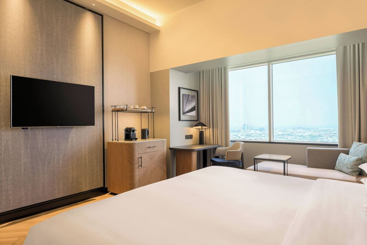 Een moderne hotelkamer met een groot bed, een bureau, een stoel, een televisie en een raam met uitzicht op de stad.