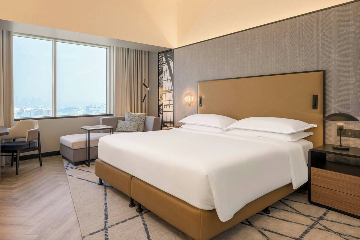 Een hotelkamer met een groot bed, een bureau, een stoel, een klein tafeltje en uitzicht op de stad.