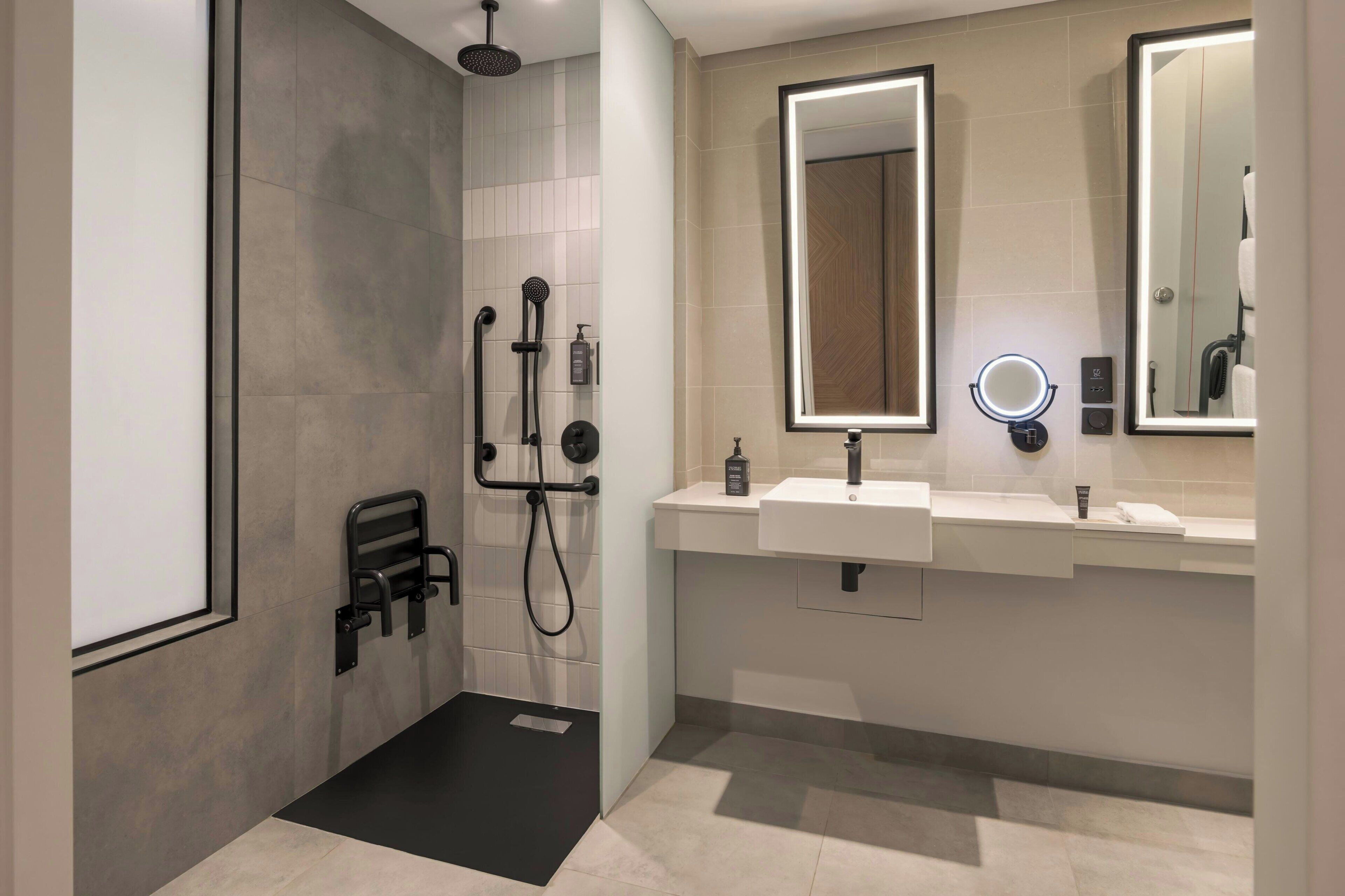 A modern bathroom with a shower, two sinks, and large mirrors.