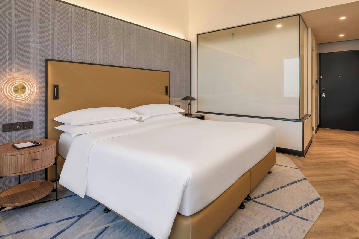 Een moderne hotelkamer met een groot bed, een nachtkastje, een lamp en een grote spiegel.