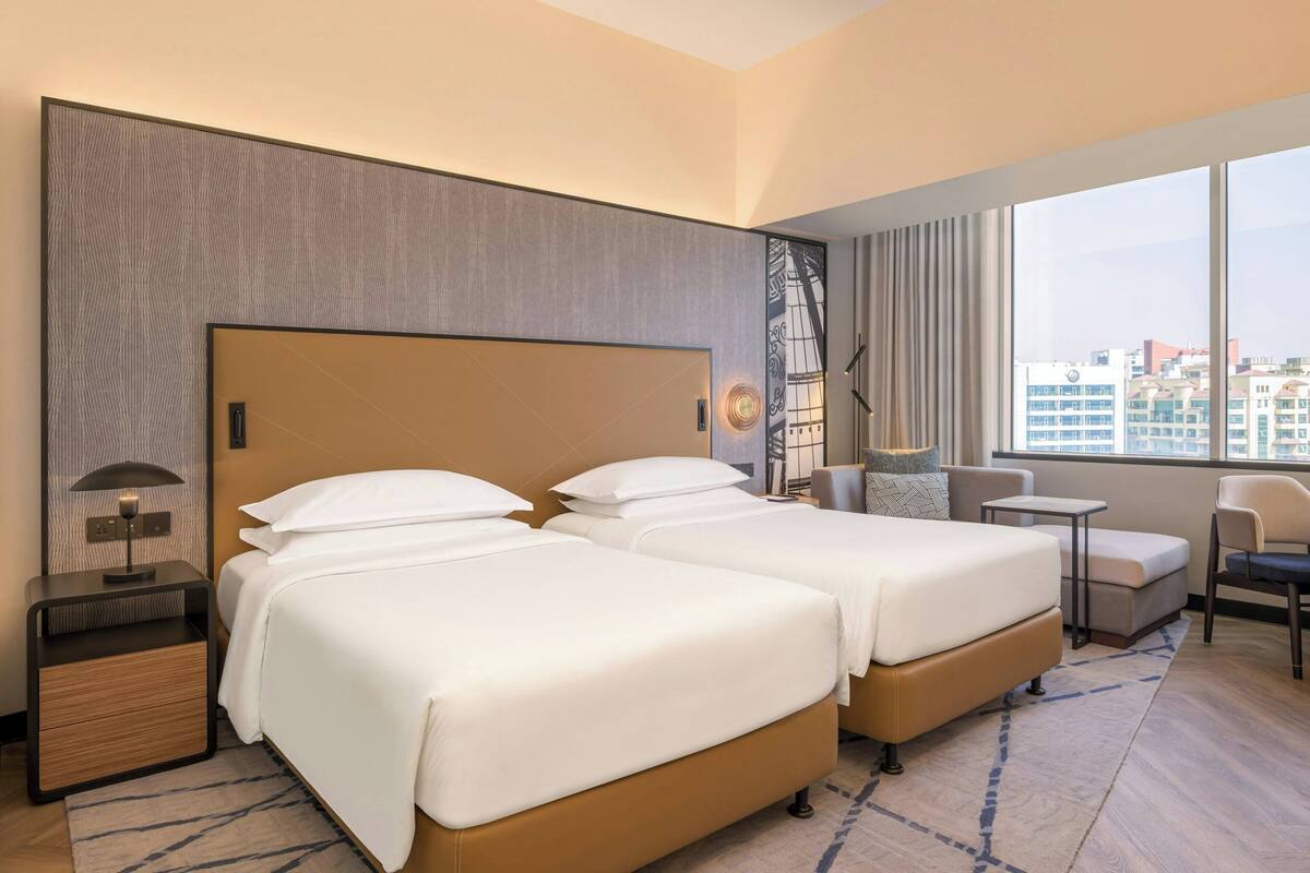 Een hotelkamer met twee bedden, een tafeltje, een stoel en uitzicht op de stad.