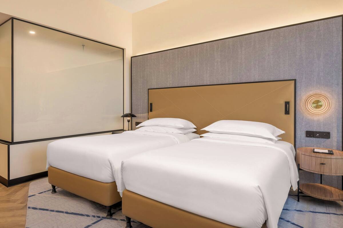 Een hotelkamer met twee bedden, een grote spiegel, een nachtkastje en een wandlamp.