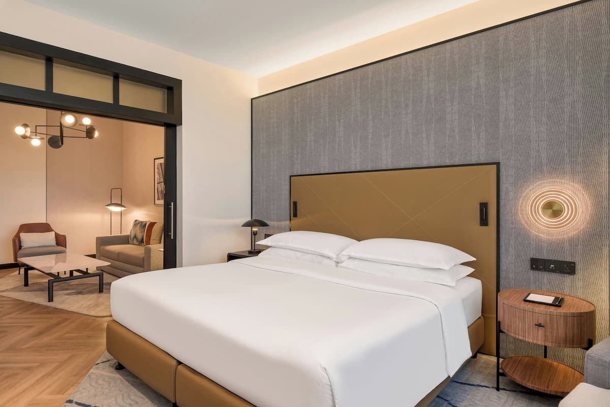 Een moderne hotelkamer met een groot bed, een zithoekje met een tafeltje en een nachtkastje met een lamp.