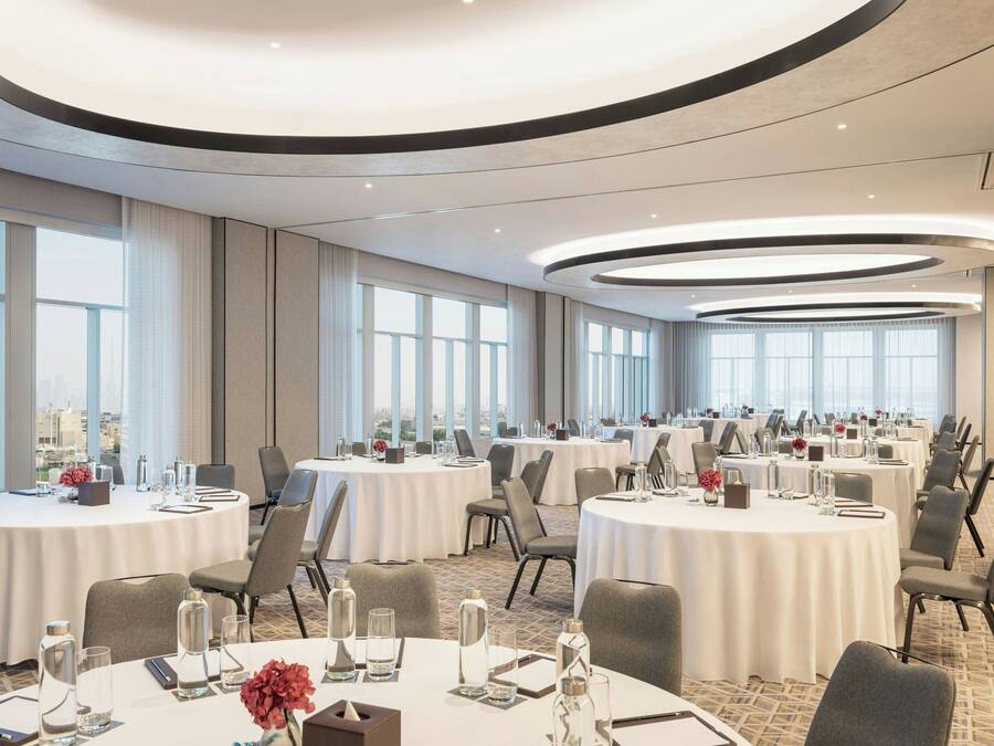 Un salón de conferencias con varias mesas redondas, ventanas amplias y vista a la ciudad.