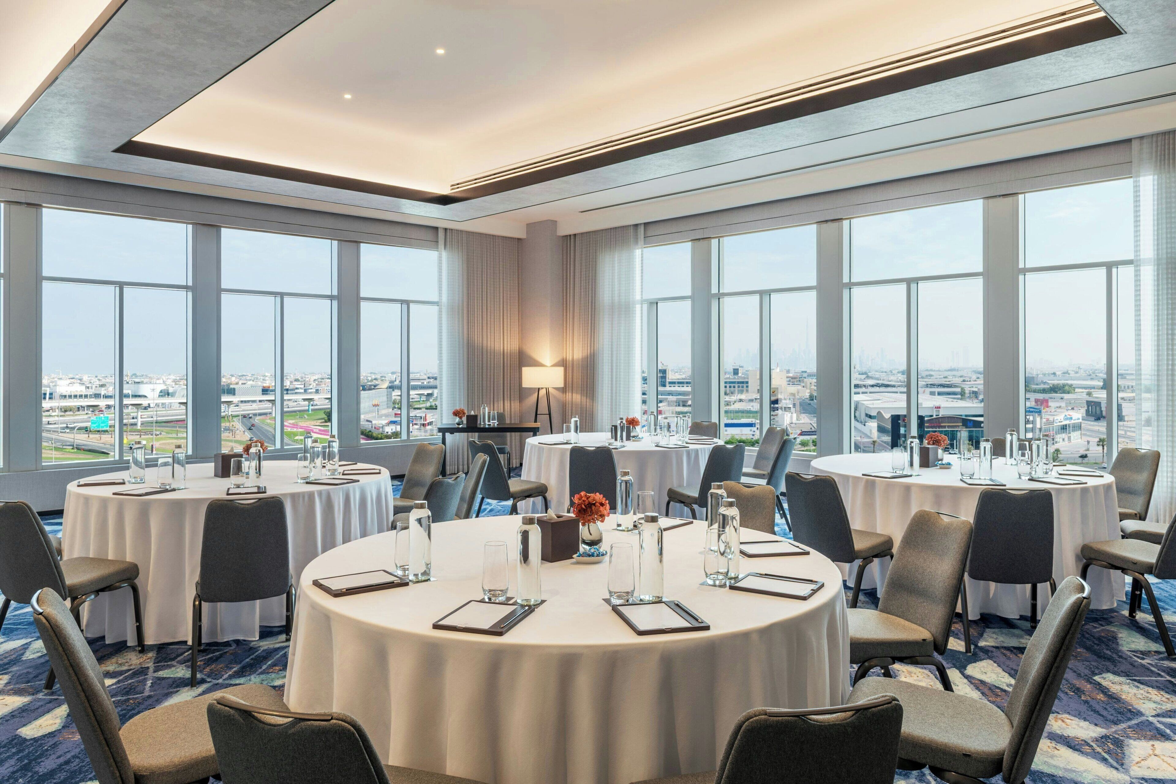 A conference room with round tables, chairs, and a city view through large windows.