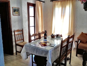 A dining area with a glass table, wooden chairs, a bottle of wine, and a bowl of bread. - Filoxenia Villa (Ierapetra)