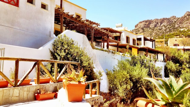 Un edificio blanco con balcones, rodeado de macetas con plantas y un paisaje montañoso al fondo.