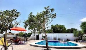 A swimming pool with a tiled deck, surrounded by lounge chairs and a red umbrella. - Filoxenia Villa (Ierapetra)