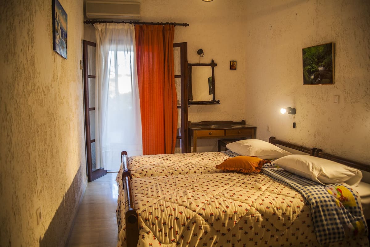 A bedroom with a bed, a nightstand, a mirror, and a window with curtains.