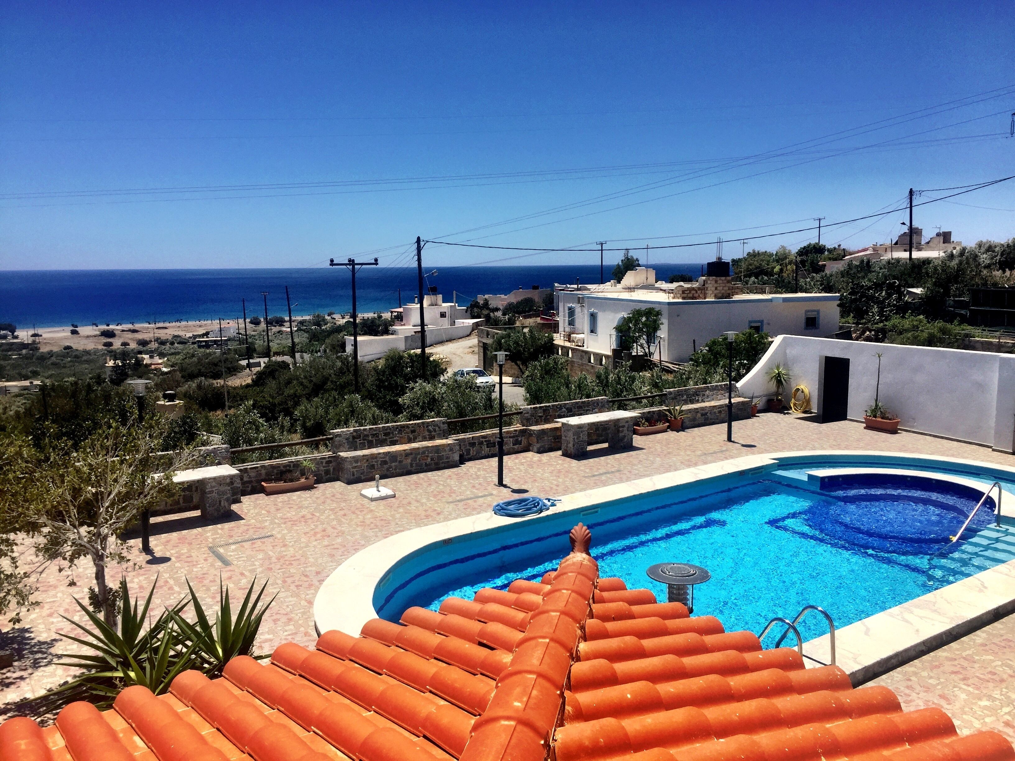 Una piscina de borde curvo, rodeada por una terraza de piedra y sillas reclinables color naranja.