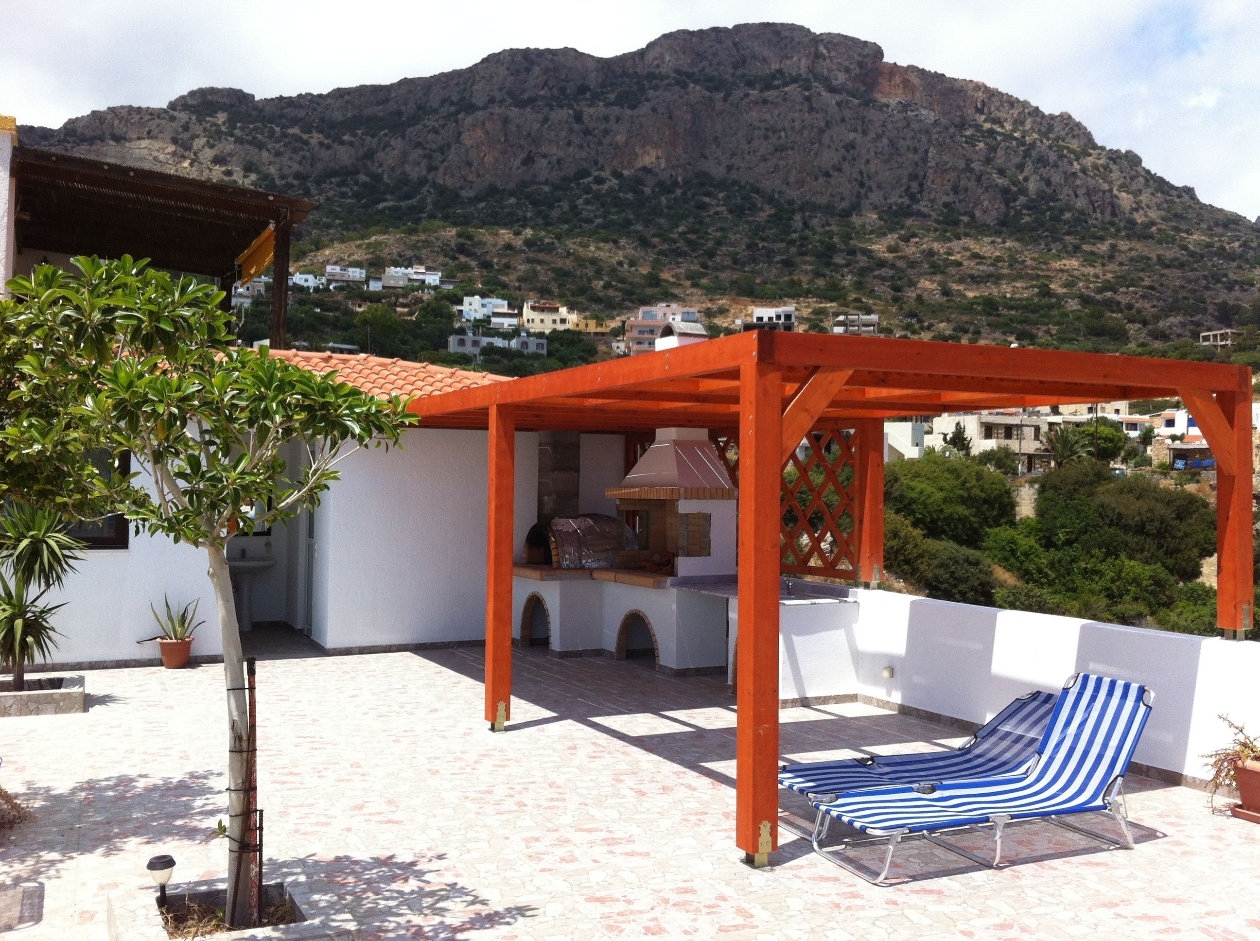 A rooftop patio with a wooden pergola, a barbecue area, and a striped lounge chair.