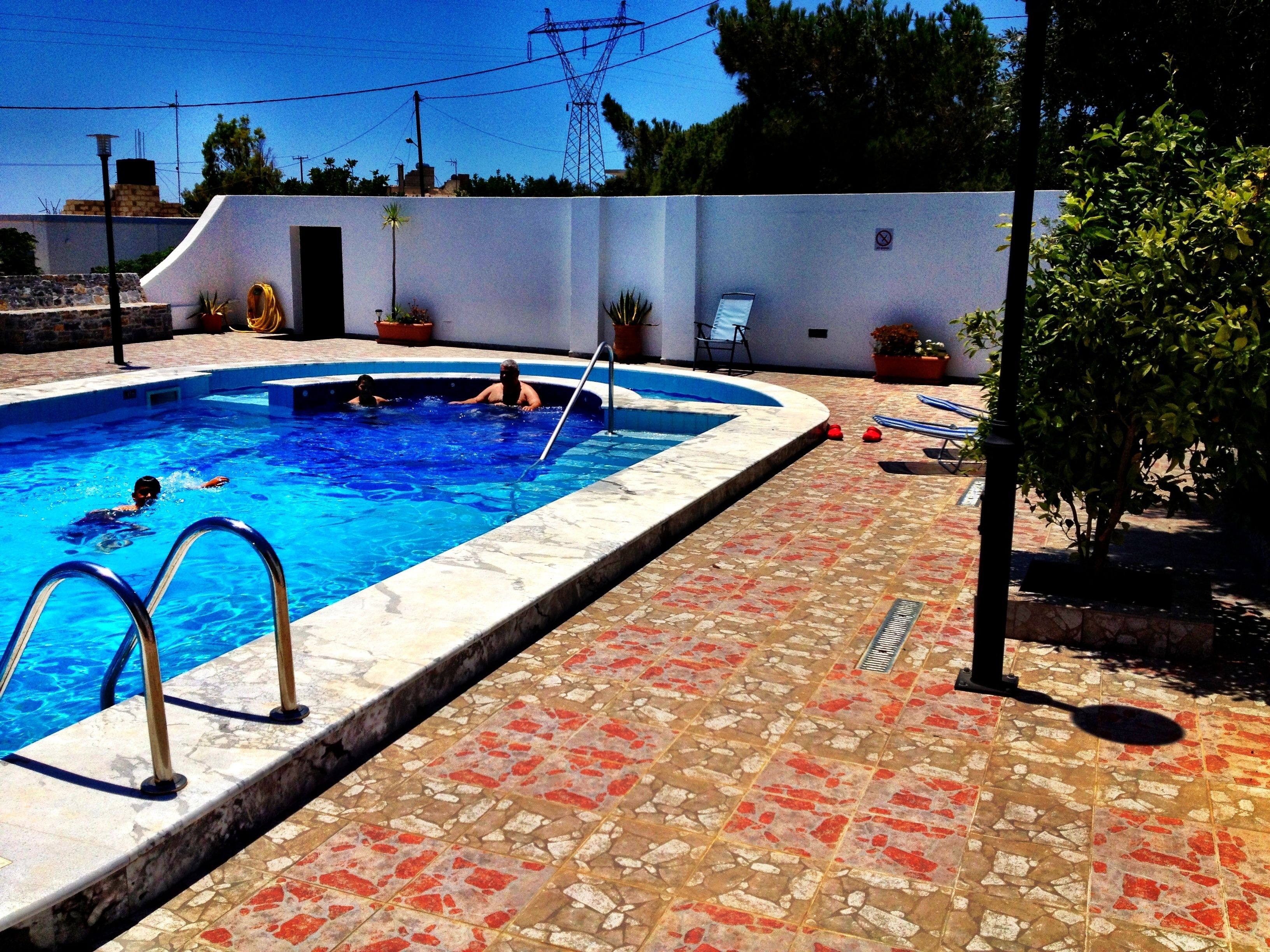 A swimming pool with a tiled deck, a ladder, and a few people swimming.