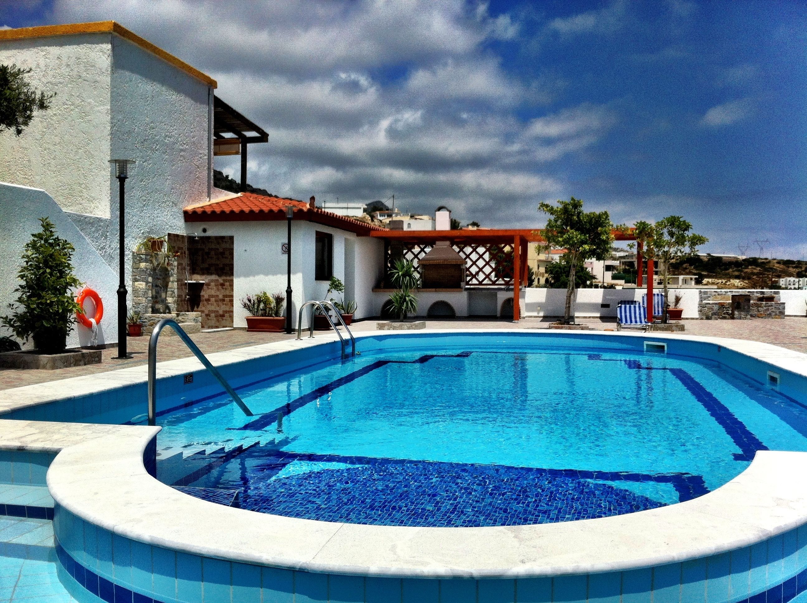 A swimming pool with a tiled edge, a covered seating area, and potted plants.