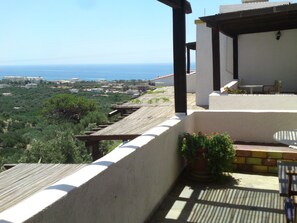 Una terraza con vistas al mar, pérgola de madera y zona de estar con mesa y sillas.