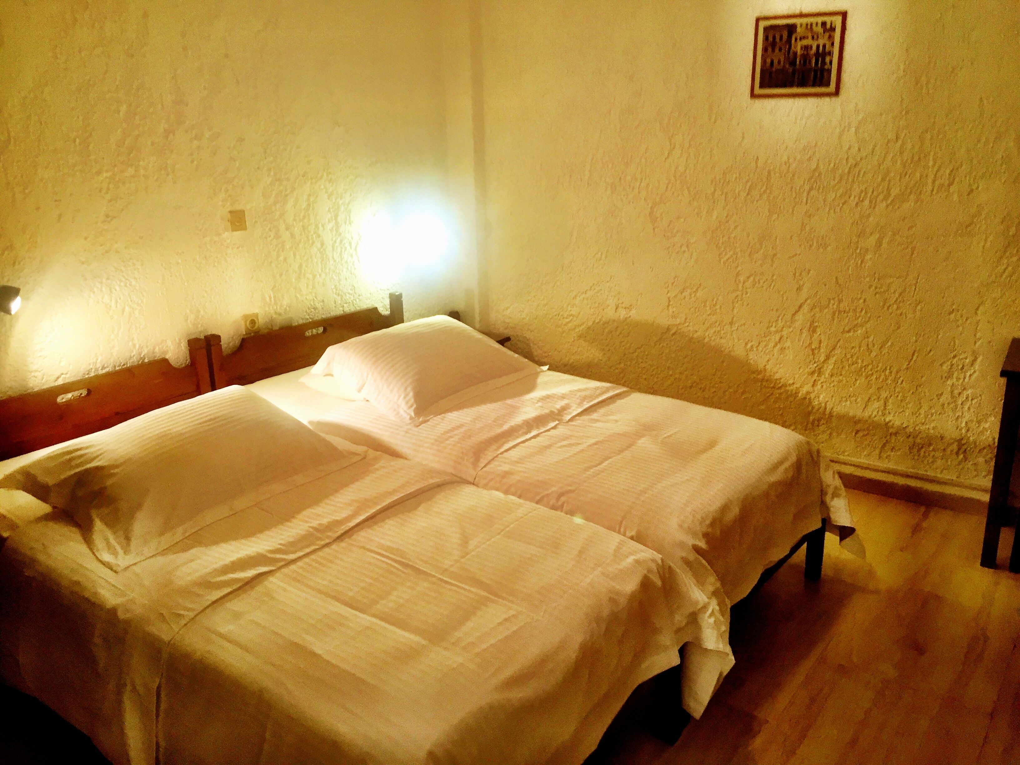 A room with two single beds, wooden headboards, a small framed picture on the wall, and a wooden floor.