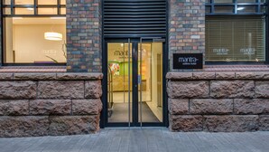 A hotel entrance with glass doors, a brick facade, and signage for 'Mantra Collins Hotel'.