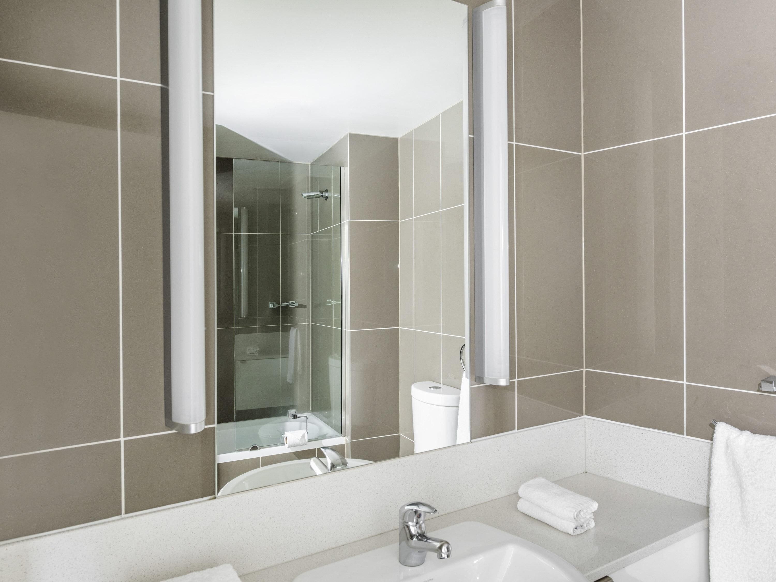 A modern bathroom with a large mirror, a sink, and a shower.