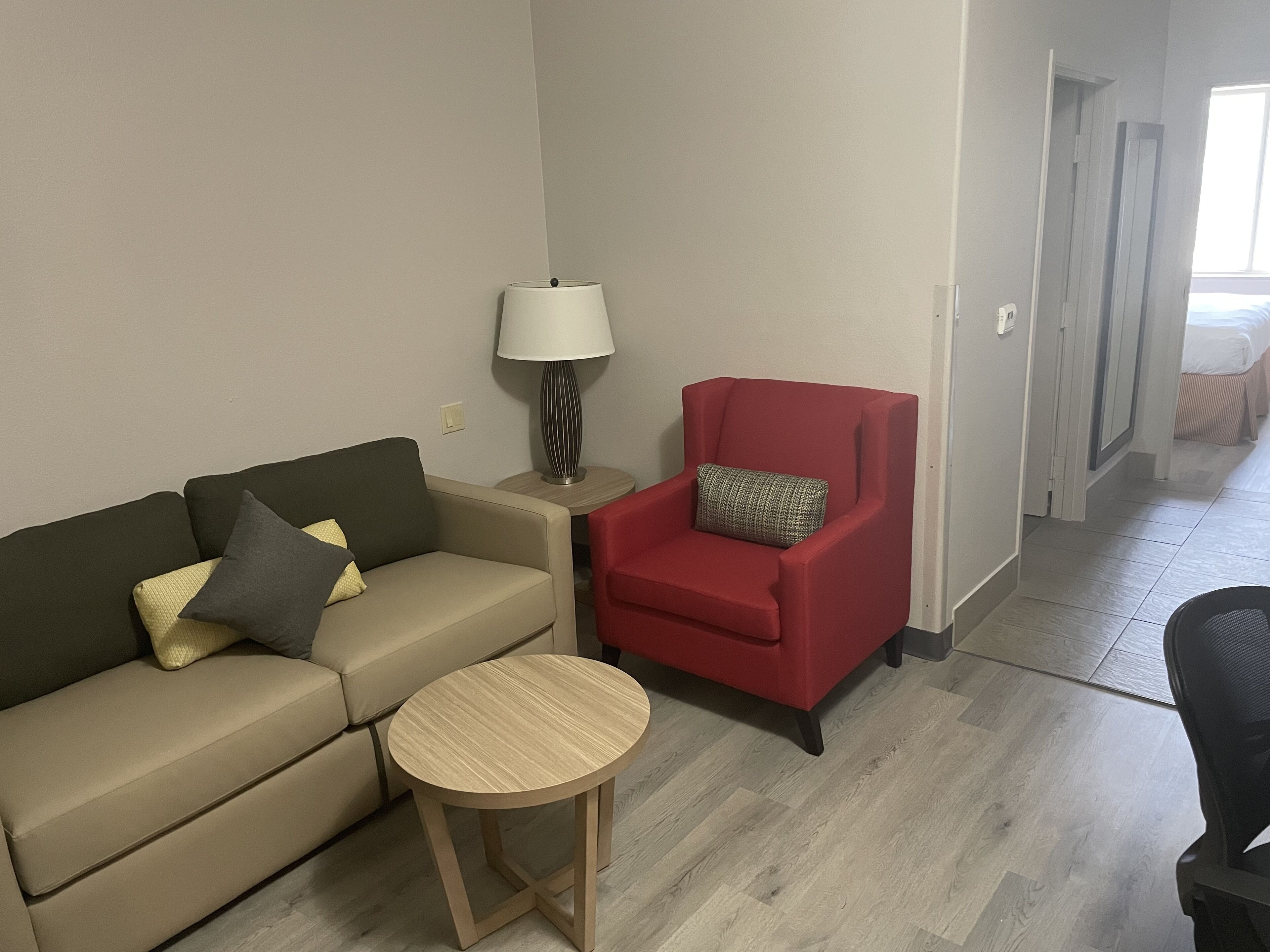 Una sala de estar moderna con un sofá color beige, un sillón rojo, una mesita de madera y una lámpara de pie.