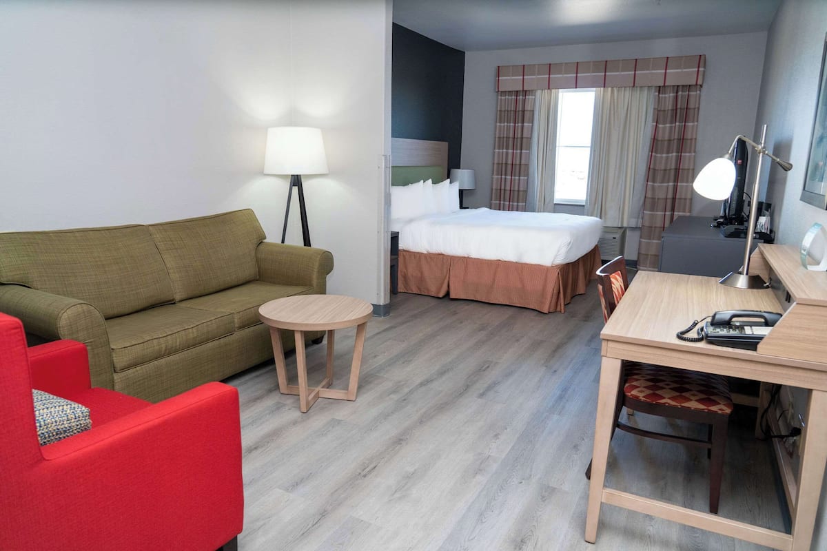 Hotellihuone, jossa on sänky, työpöytä tuolilla, pieni pyöreä pöytä, punainen nojatuoli ja lamppu.