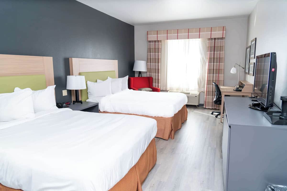 Hotellihuone, jossa on kaksi sänkyä, työpöytä, tuoli, televisio ja ikkuna, jossa on verhot.