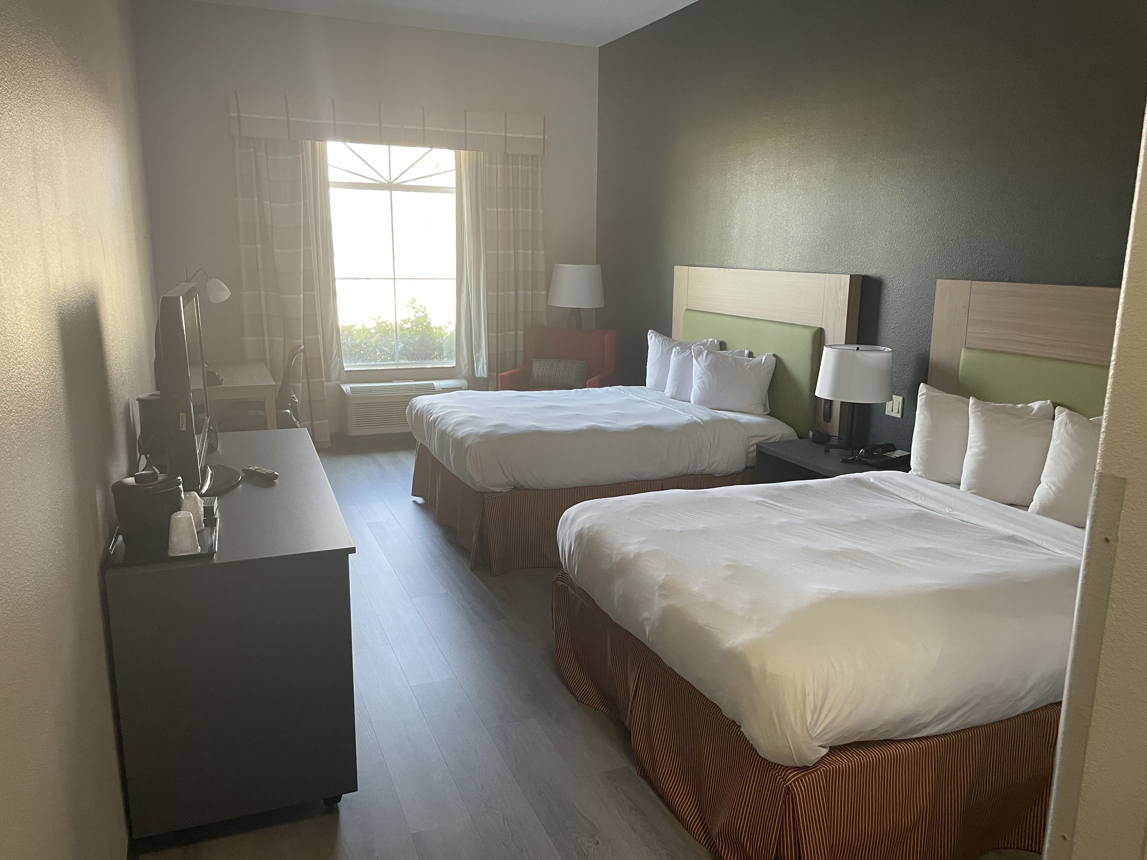 Une chambre d’hôtel avec deux lits, un bureau, une chaise et une fenêtre avec des rideaux.