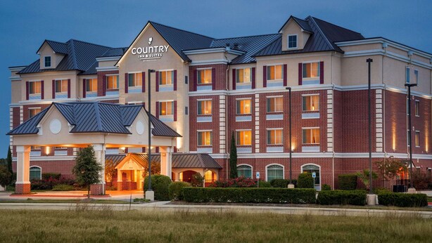 A Country Inn & Suites building with a brick facade, multiple windows, and a well-lit entrance. - Country Inn & Suites by Radisson, College Station, TX (College Station)