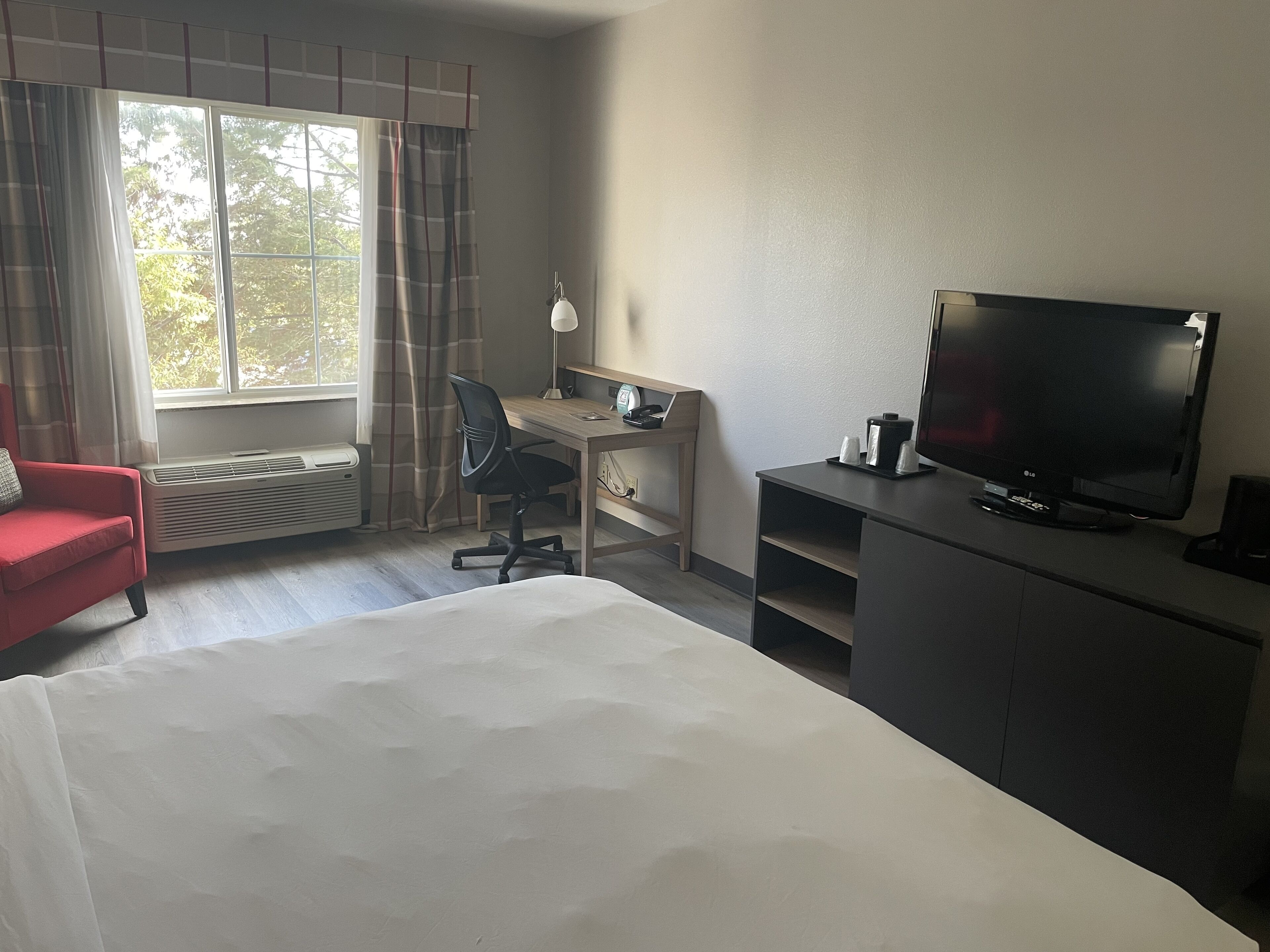 Ein Hotelzimmer mit Bett, Schreibtisch mit Stuhl, Fernseher und einem roten Sessel.