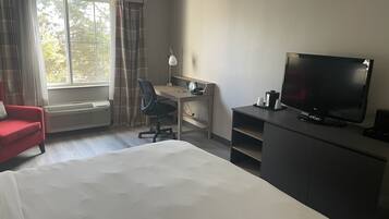 Ein Hotelzimmer mit Bett, Schreibtisch mit Stuhl, Fernseher und einem roten Sessel.