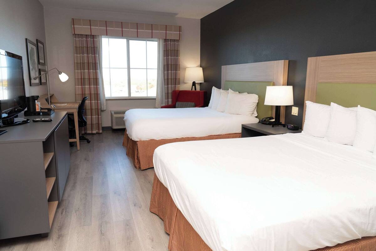 Hotellihuone, jossa on kaksi sänkyä, työpöytä, tuoli, televisio ja ikkuna, jossa on verhot.