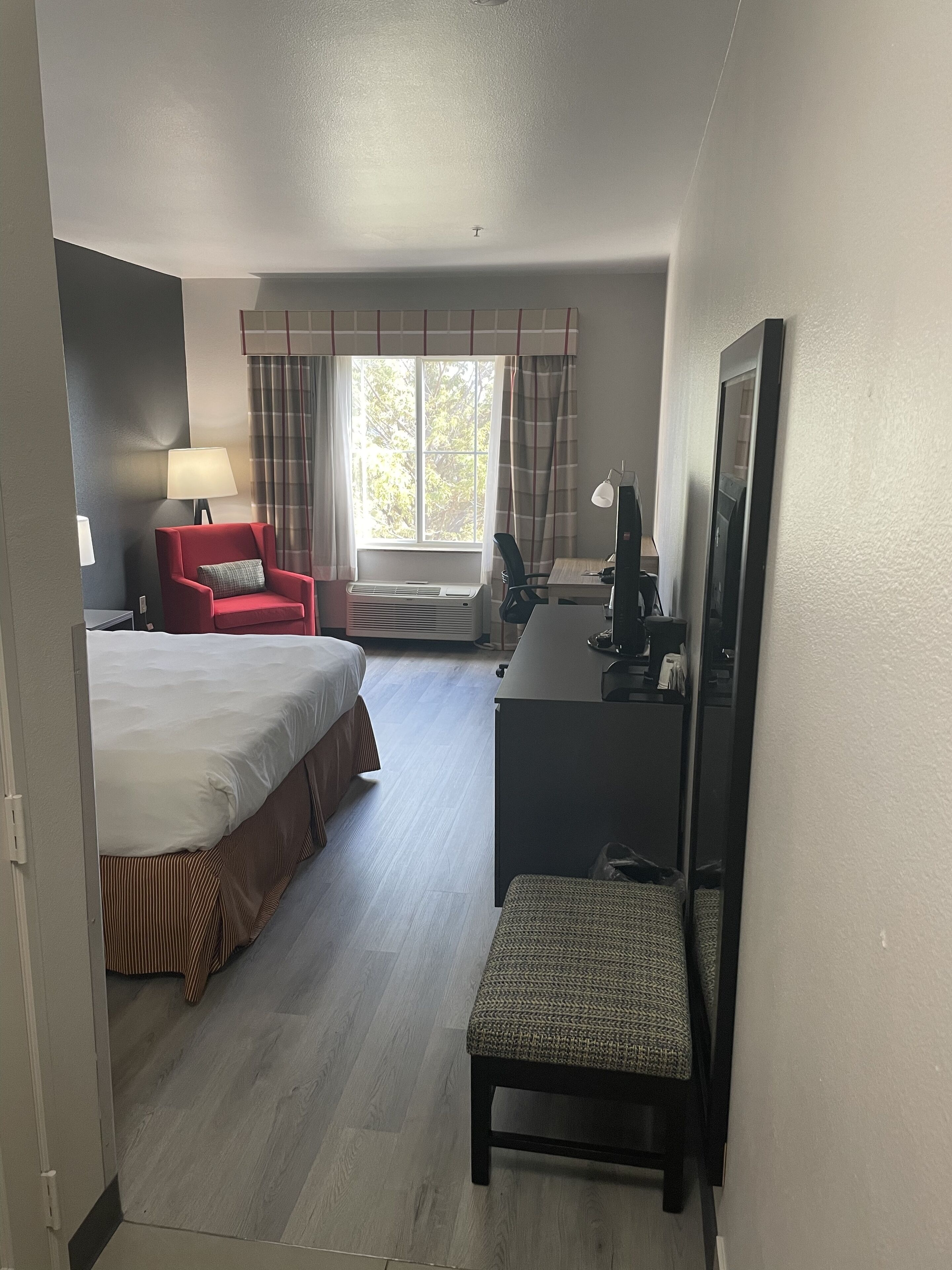 Ett hotellrum med en säng, ett skrivbord, en stol, en lampa och ett fönster med gardiner.