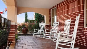 A covered patio with white rocking chairs and a brick wall. - Country Inn & Suites by Radisson, College Station, TX (College Station)