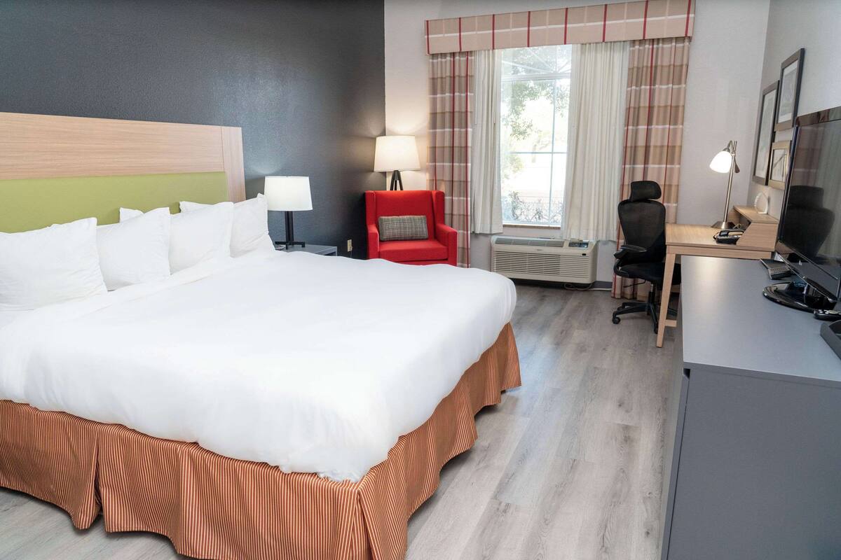 Hotellihuone, jossa on suuri sänky, työpöytä tuolilla, punainen nojatuoli ja televisio.