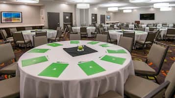 Un salón de conferencias con mesas redondas, sillas y una mesa central con una carpeta verde.