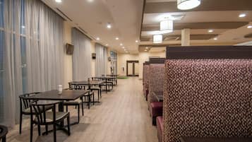 A hotel dining area with tables and booths, a patterned wall, and a ceiling with recessed lighting.