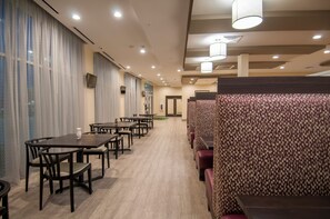 Comedor de hotel con mesas y cabinas, un muro con diseño y un techo con iluminación empotrada.