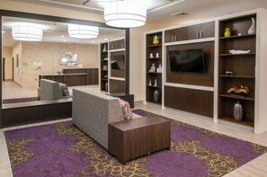 Eine moderne Hotelhalle mit einer Rezeption, einer Sitzecke und einem großen Bildschirm.