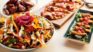 Variedad de platillos como nachos, pizza y comida frita sobre una mesa.