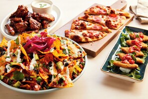 Variedad de platillos como nachos, pizza y comida frita sobre una mesa.