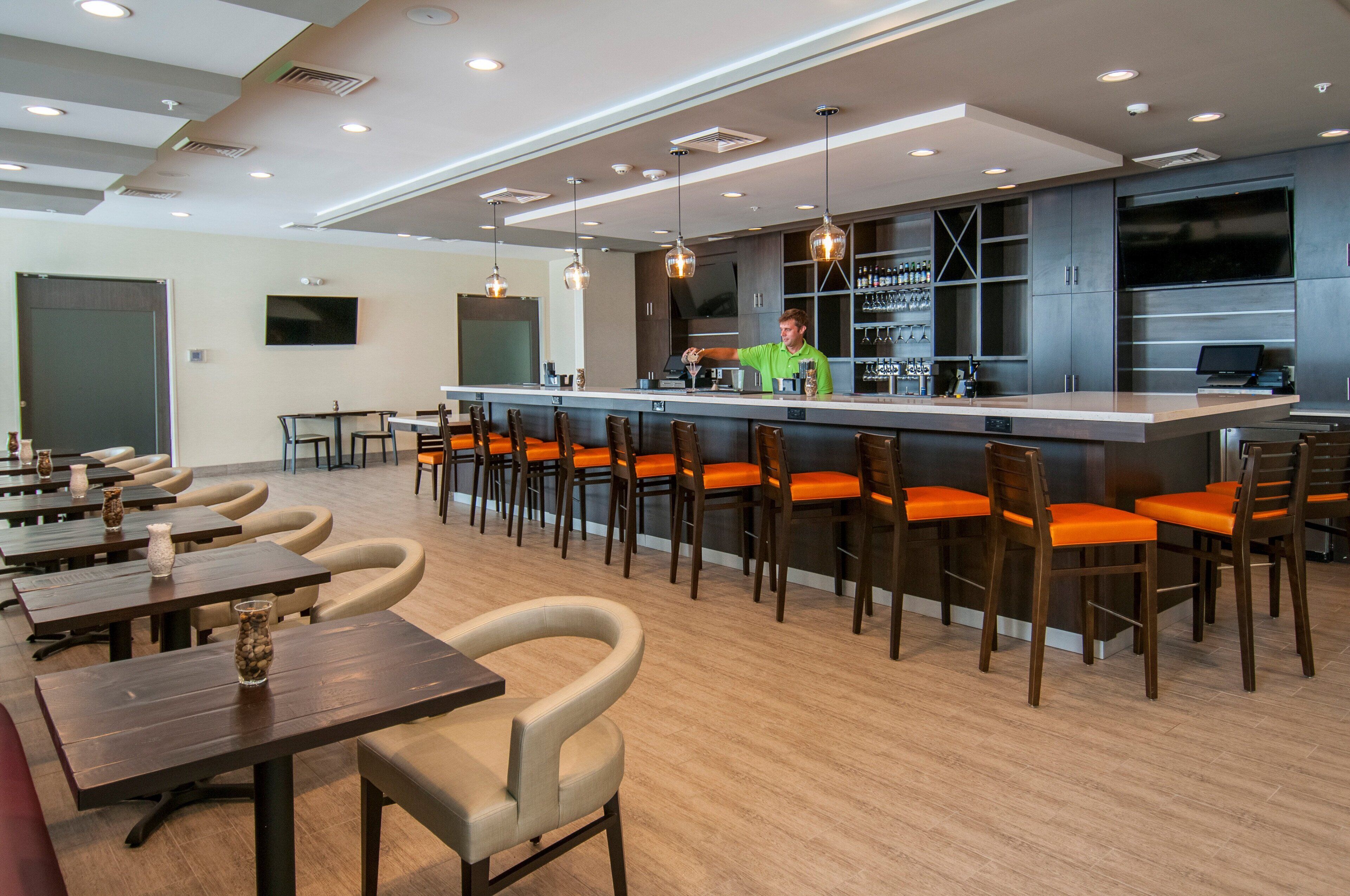 A modern bar area with a long counter, multiple bar stools, and a television mounted on the wall.