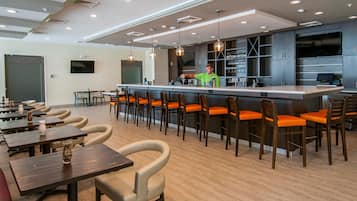 Un área de bar moderna con una barra alargada, varios taburetes y un televisor montado en la pared.