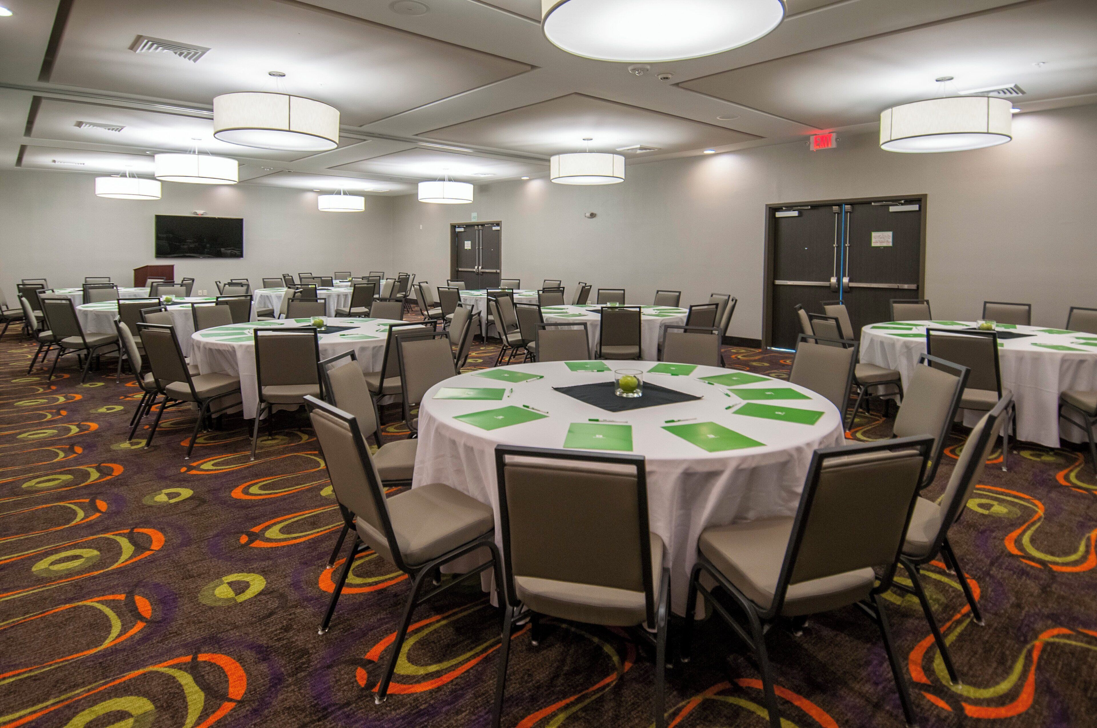 A conference room with multiple tables and chairs, equipped with nameplates and folders, in a hotel setting.