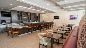 A modern restaurant with a bar area, multiple seating options including booths and tables, and a large TV screen.